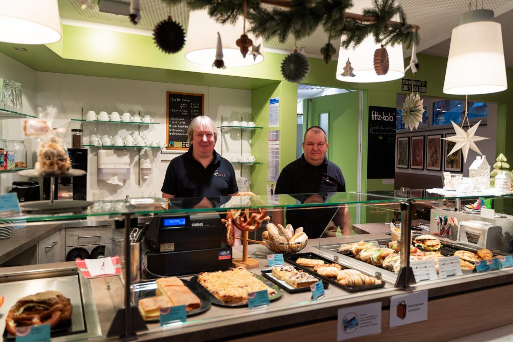 Zwei Mitarbeiter bei der Arbeit im Cafe. Sie stehen vor der Auslage und neben ihrer Kasse während der Weihnachtszeit