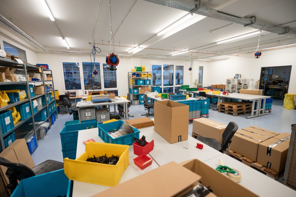 Mehrere blaue und graue Boxen, Europaletten und Kartons in einer gutbeleuchteten Werkstatt