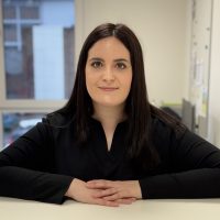 Dunkelhaarige Mitarbeiterin im schwarzen Pullover steht an einem Tresen